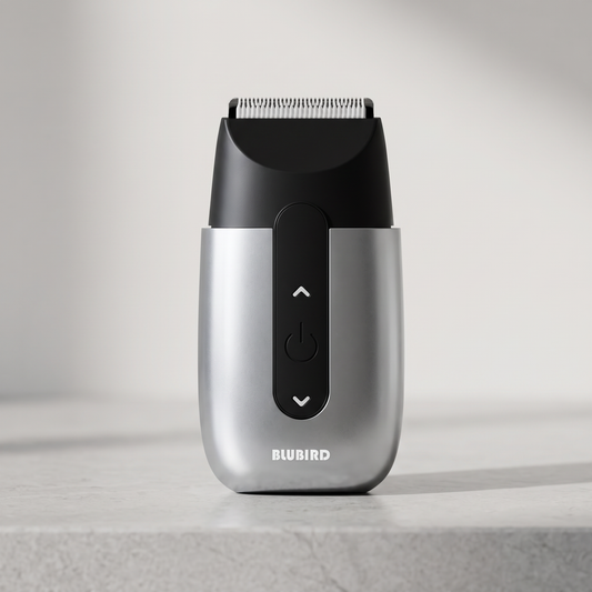 Blubird Hummingbird single-head rotary shaver standing on a pale stone bathroom counter in cool neutral daylight, BLUBIRD wordmark visible on the silver front of the device body