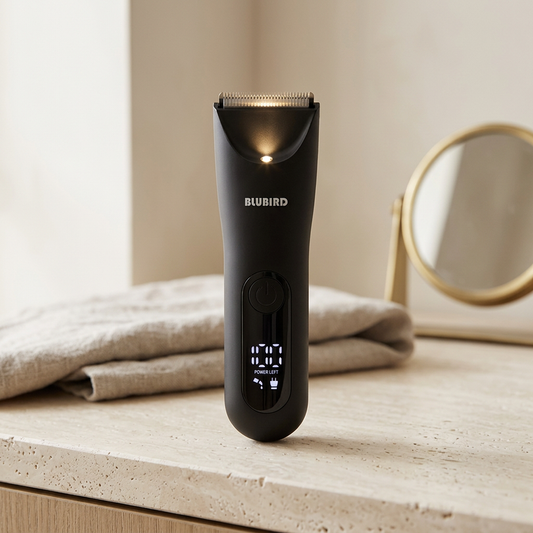 a black Blubird Trim Reaper body trimmer standing upright on a pale stone bathroom vanity in morning light with its LED light glowing beside a folded linen towel