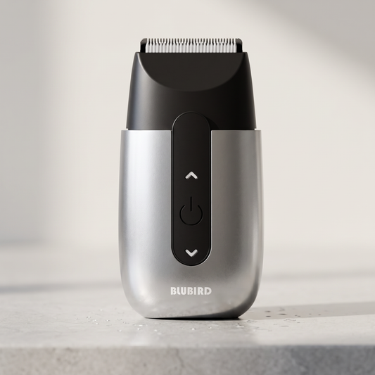 A Blubird Hummingbird electric shaver standing upright on a pale grey stone bathroom counter in cool morning light, BLUBIRD wordmark visible on the front of the silver body
